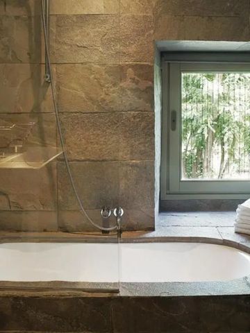 Steinverkleidetes Badezimmer mit eingelassener Badewanne und großem Fenster.
