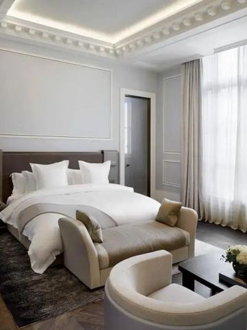 Helles Hotelzimmer mit großem Bett, Sitzgelegenheiten und hohen Fenstern