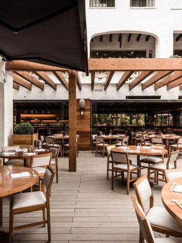 Restaurant mit Holzmöbeln im Freien unter einer Pergola in einem luxuriösen Hotel.