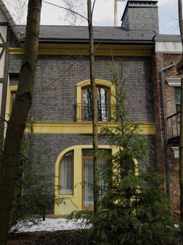 Gebäude mit grauem Mauerwerk und gelben Fenstereinfassungen hinter Bäumen.