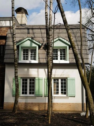 Charmantes Gebäude mit grünen Fensterläden und Dachgauben umgeben von Bäumen