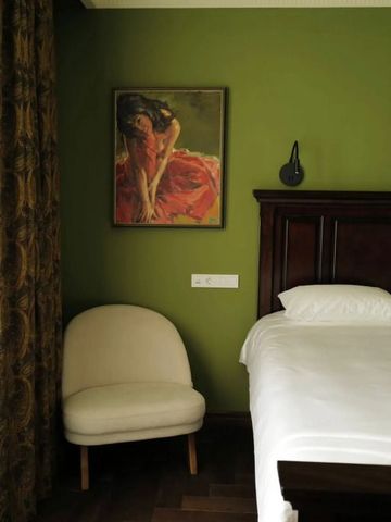 Hotelzimmer mit grün gestrichenen Wänden und Kunstwerk über einem luxuriösen Bett