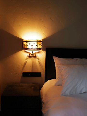 Gemütlich beleuchtetes Bett mit kunstvoller Wandlampe im Schlafzimmer