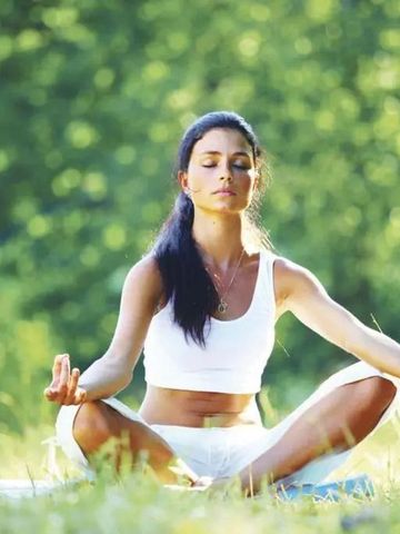 Frau praktiziert Yoga in einem grünen, sonnigen Garten