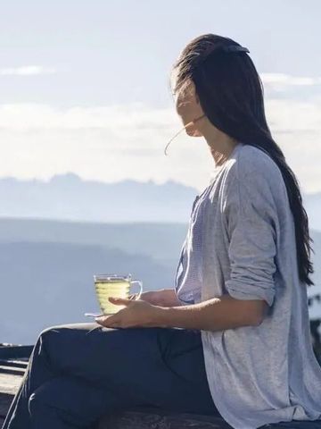 Frau genießt eine Tasse Tee auf einer Terrasse mit Bergblick