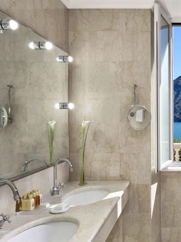 Badezimmer mit Marmorverkleidung und Seeblick durch große Fenster.