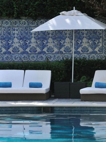 Sonnenliegen und Sonnenschirm am Pool vor traditioneller blauer Kachelwand