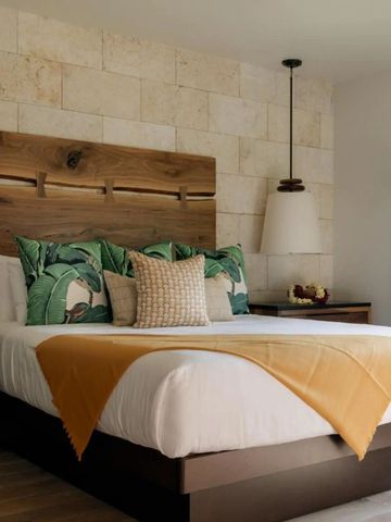 Hotelzimmer mit Holzbett, Zierkissen und Pflanzenmotiv