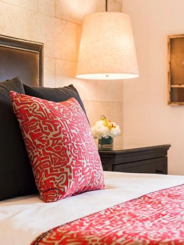 Nahaufnahme eines Hotelbetts mit rotem Zierkissen und passender Decke