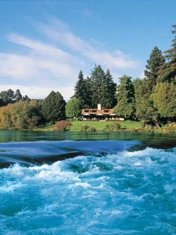 Naturkulisse mit Fluss und bewaldetem Ufer vor einem eleganten Gebäude.