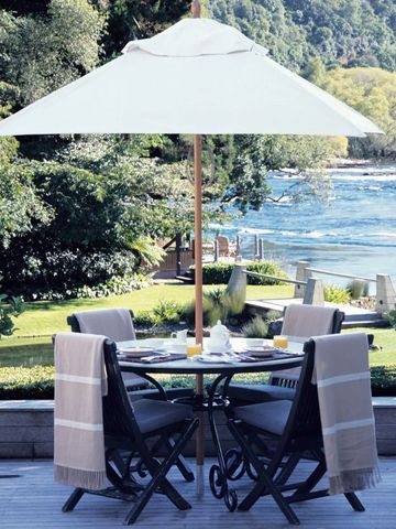 Terrasse mit Tisch und Stühlen unter weißem Sonnenschirm mit Blick auf den Fluss.