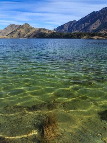 Kristallklares Wasser eines Sees mit umliegenden Bergen unter einem blauen Himmel