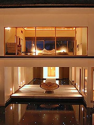 Beleuchtete Villa bei Nacht mit großem Fenster und Wasseransicht im Vordergrund