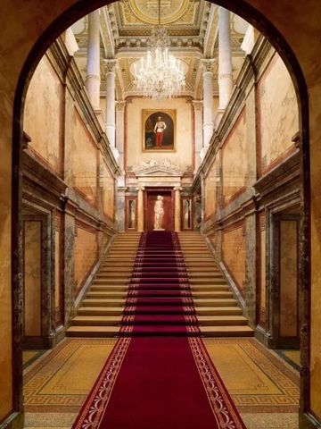 Prunkvolle Treppe mit rotem Teppich und Gemälden an den Wänden