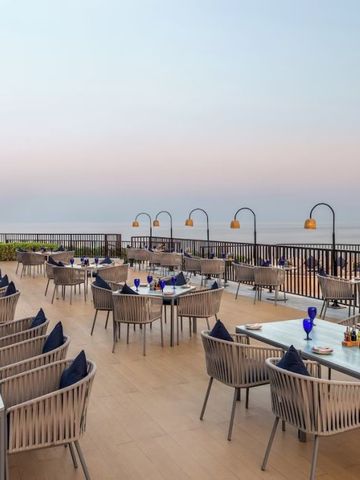 Terrasse mit Esstischen und Blick aufs Meer bei Sonnenuntergang