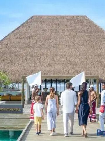 Gäste auf einem Steg vor einem strohgedeckten Gebäude mit traditioneller Inselkleidung.