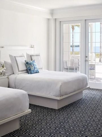 Helles Hotelzimmer mit zwei Betten und Zugang zum Balkon mit Meerblick