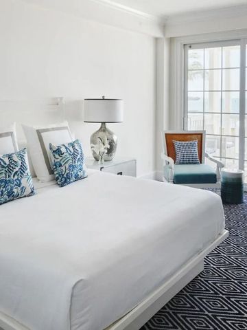 Helles Hotelzimmer mit großem Bett und Meerblick durch bodentiefe Fenster.