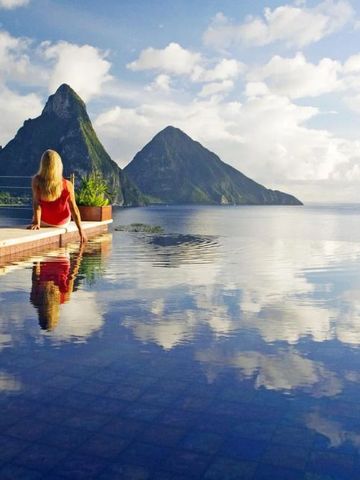 Frau genießt den Ausblick im Infinity Pool über Meer und Berglandschaft