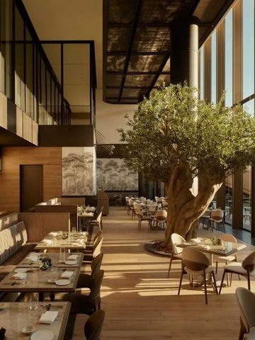 Helles Hotelrestaurant mit Innenbaum und hohen Glasfenstern