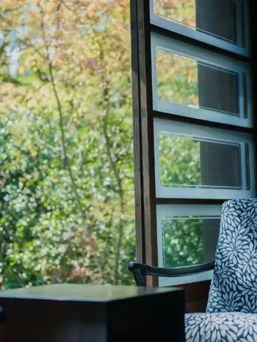 Nahaufnahme eines Sessels vor einem offenen Fenster mit Gartenblick