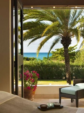 Blick von einem Zimmer auf eine Terrasse mit Palmen und Meer im Hintergrund