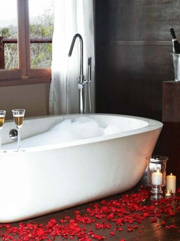 Freistehende Badewanne mit Rosenblättern und Champagner.