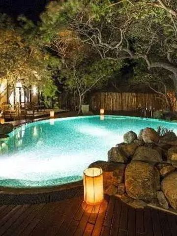 Beleuchteter Pool bei Nacht inmitten von Natur und Felsformationen