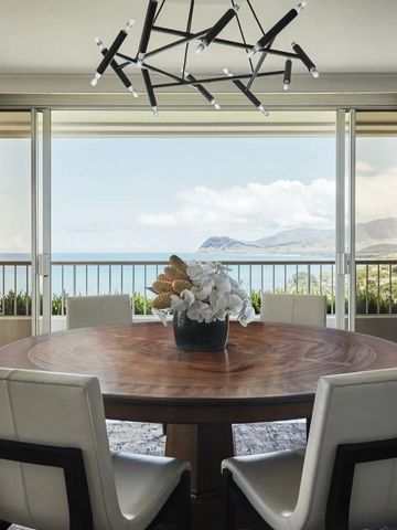 Essbereich mit großem Holztisch und weißen Stühlen, Blick auf das Meer im Hintergrund.