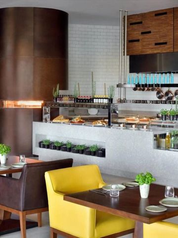 Einladendes Bistro mit offener Küche und gelben Sitzmöbeln im JW Marriott Hotel Muscat