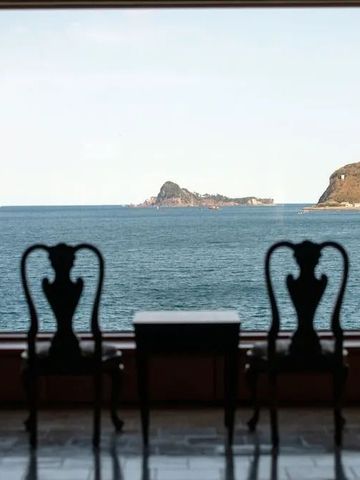 Panoramafenster mit Meerblick und zwei stilvollen Stühlen im Vordergrund