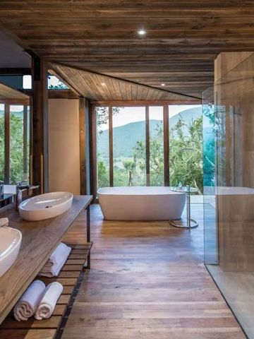 Luxuriöses Badezimmer mit freistehender Badewanne und Panoramafenster mit Naturblick