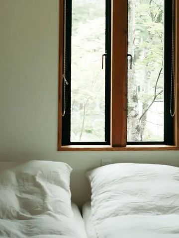 Einfaches Schlafzimmer mit Blick auf grünes Waldgebiet durch ein schmales Fenster
