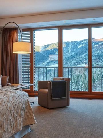 Hotelzimmer mit breitem Fenster, Blick auf verschneite Berglandschaft.