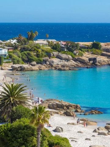 Blick auf einen sonnigen Strand mit klarem Wasser und grüner Landschaft.