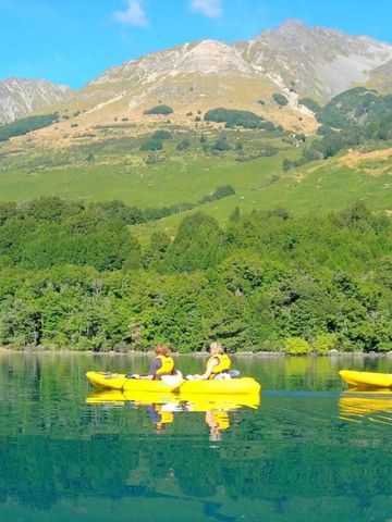 Personen in gelben Kajaks auf einem ruhigen See vor Bergkulisse