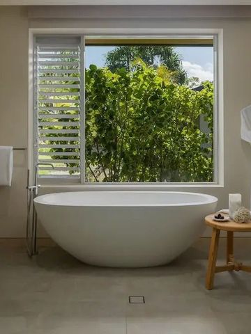 Freistehende Badewanne mit Blick auf tropisches Grün durch das Fenster