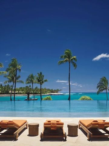 Sonnenliegen am Rand eines Infinity-Pools mit blauem Himmel und Meer