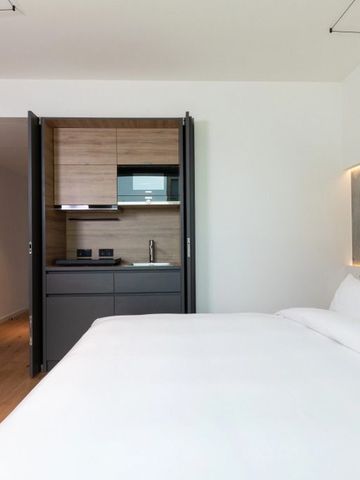 Helles Hotelzimmer mit Doppelbett und integrierter Küchenzeile in heller Holzoptik