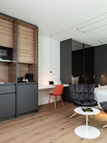 Modern ausgestattetes Hotelzimmer mit Küchenzeile und gemütlichem Sessel