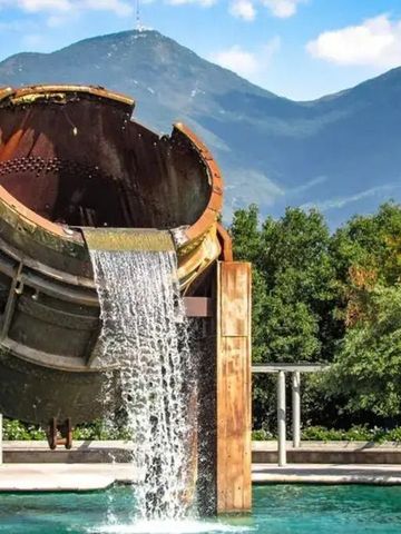 Wasserfall aus großer Eisenkonstruktion vor Berglandschaft