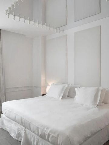 Weißes Schlafzimmer mit Doppelbett und subtilen Wandverzierungen.