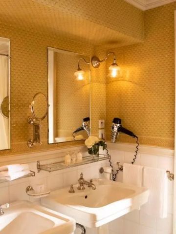 Gut beleuchtetes Badezimmer mit Doppelwaschbecken und goldener Tapete