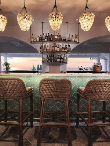 Bar mit hohen Hockern und kunstvollen Lampen. Meerblick im Hintergrund