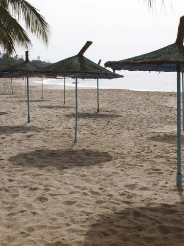 Strand mit Strohdach-Sonnenschirmen und Palmen im Hintergrund