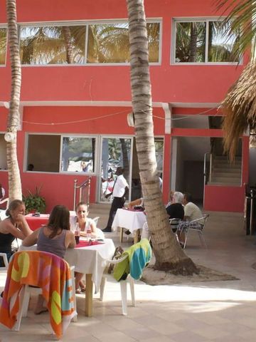 Gäste auf einer Hotelterrasse in der Nähe eines rosafarbenen Gebäudes.