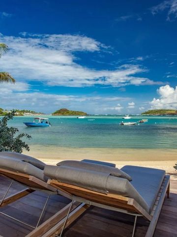 Sonnenliegen am Strand mit Blick auf türkisblaues Wasser und Boote