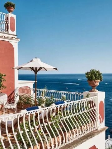 Terrasse mit Blick auf das Meer und weißen Möbeln unter einem Sonnenschirm.