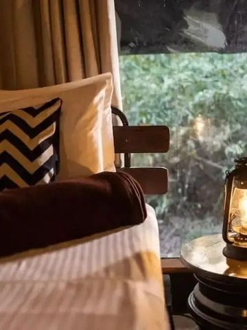 Detailaufnahme von Bett mit Lampe vor einem Fenster mit Blick ins Grüne