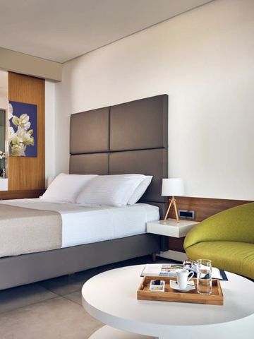 Modernes Hotelzimmer mit großem Bett, grünem Sessel und dekorativen Elementen